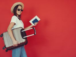 happy female traveler with suitcase on red background
