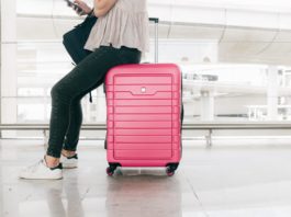 woman in white top and denim jeans sitting on red luggage bag