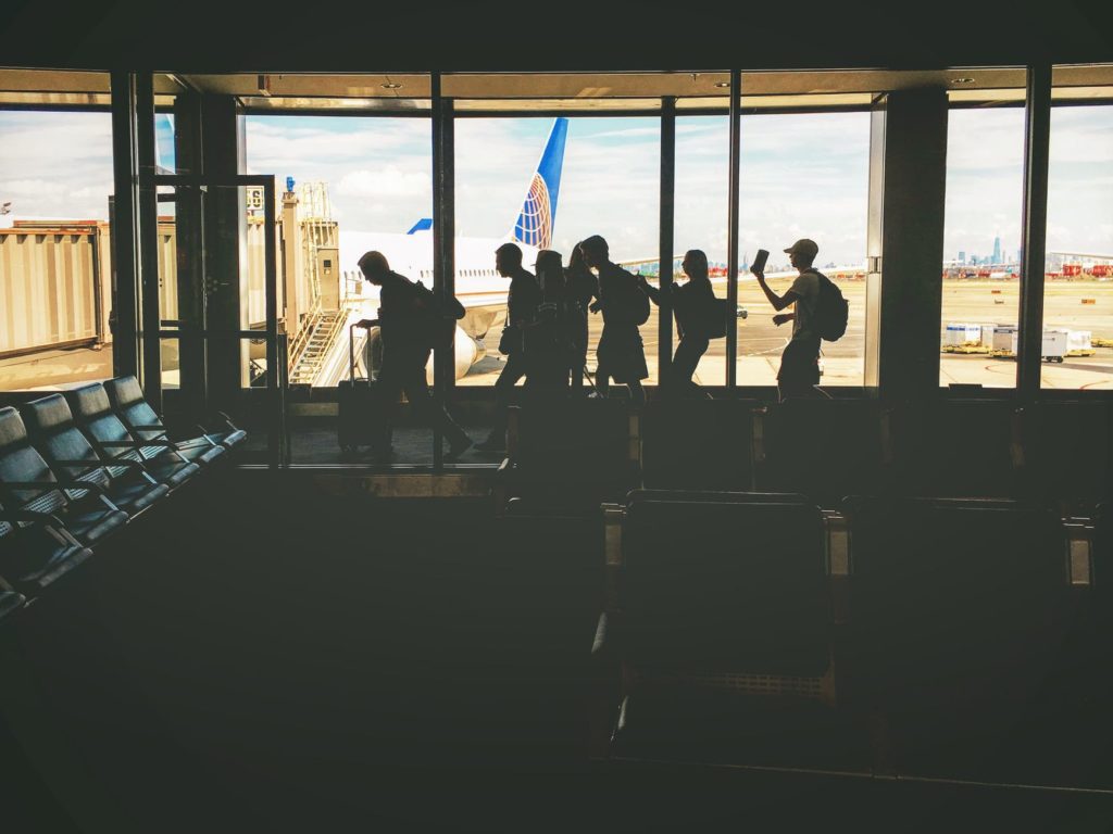 group of people walking near clear glass window with a view of white airplane parked during daytime